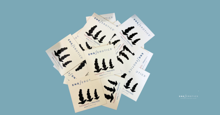 A pile of white cards with the text "ENG/erotics" and "Thoughts & Prayers" printed on them, featuring a black silhouette of three bulbous shapes, arranged on a teal background. The cards are stacked unevenly, with the brand name "ENG/erotics" visible on multiple cards.