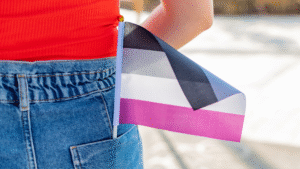 Small Asexual Pride flag (black, gray, white, magenta stripes) tucked into the back pocket of blue jeans.