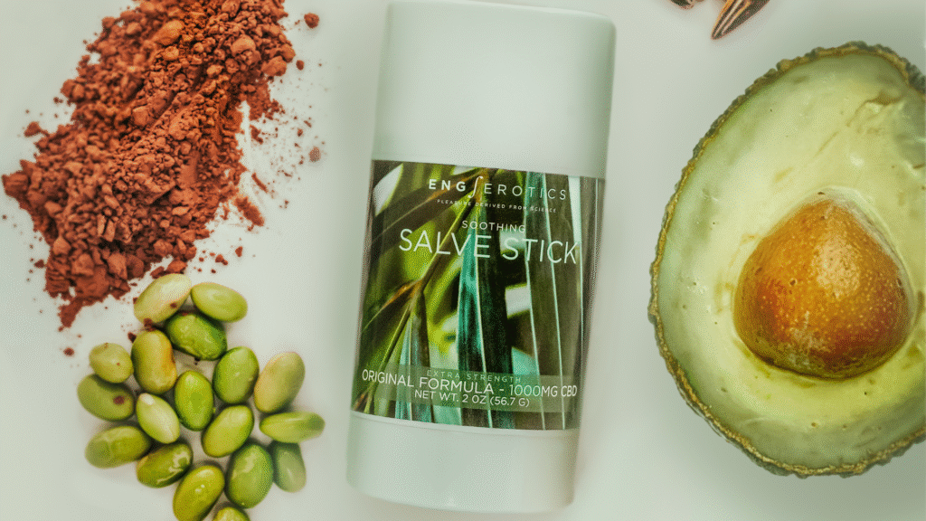 Flat lay of white Salve Stick with cocoa powder, green edamame, and half an avocado on a bright white surface.