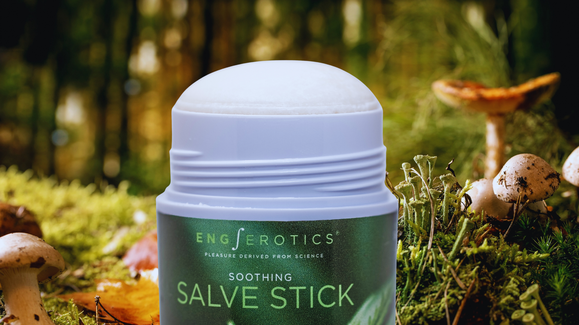 Close-up of white Soothing Salve Stick in an open tube against a blurred background of moss and wild mushrooms.